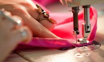 Gros plan sur une machine à coudre en action avec une main guidant le tissu rose.