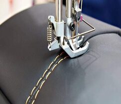 Machine à coudre industrielle piquant une couture sur du cuir noir avec un fil beige.