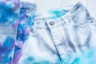 Jean teint en dégradé bleu posé sur une surface blanche, illustrant les équipements de lavage et teinture.