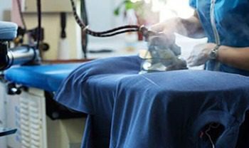 Opérateur utilisant du matériel de repassage et thermocollage sur un vêtement en tissu bleu.