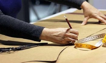 Main traçant un patron textile avec une règle et un mètre ruban sur une table de coupe.