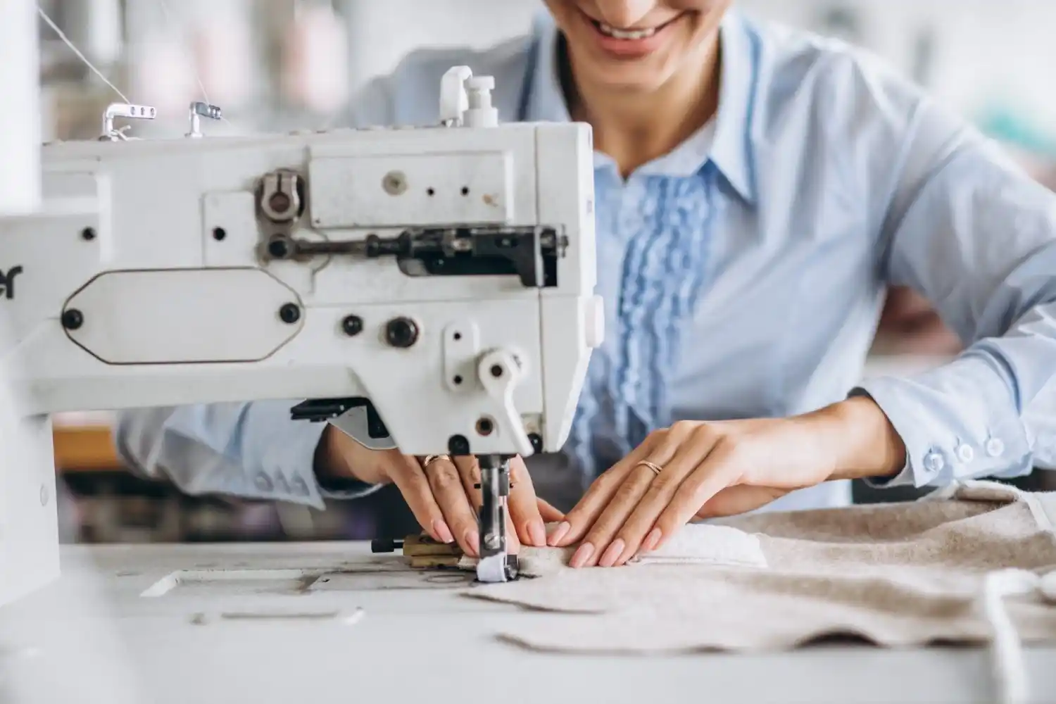 Femme en chemise bleu utilisant une machine à coudre industrielle dans un atelier de confection textile.